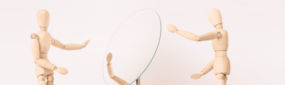 Two wooden figures, one reaching out to another who is focused on their reflection in a mirror