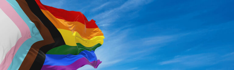 Pride flag in front of a blue sky.